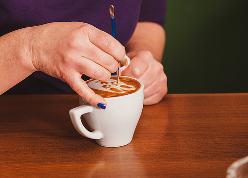 Barista making a cup of latte art coffee with special metal device - latte-art pen tool