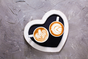 Latte art in two cups of cappuccino on the heart shape tray. Happy morning Valentine day couple