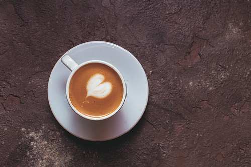 Latte art heart in cup of cappuccino. Top view on brown concrete background