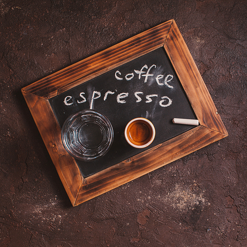 Top view of a cup of coffee and glass water on an old school slate with inscription