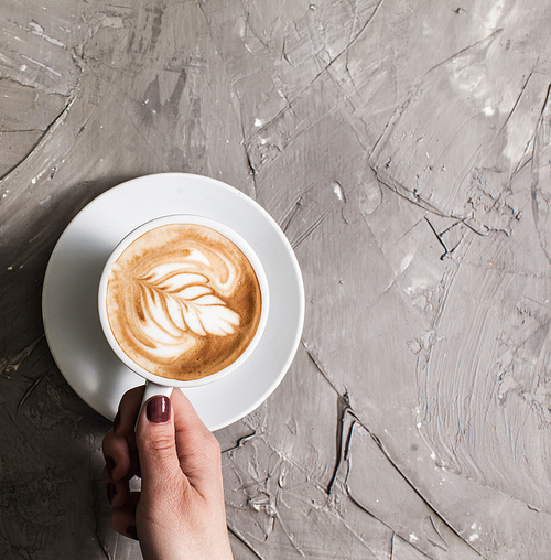Female hand holding a cup of cappuccino with figure cream. Top view with copy space