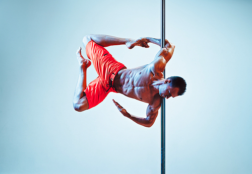 Young strong pole dancing man on wall background