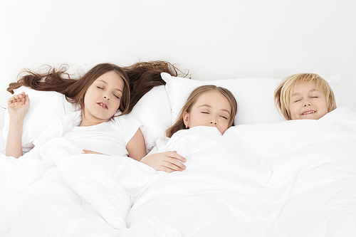 Three beautiful children sleeping in bed under one white blanket