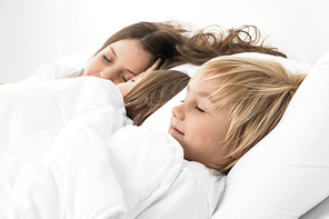Three beautiful children sleeping in bed under one white blanket