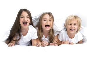 Three happy smiling children waking up in bed under one blanket