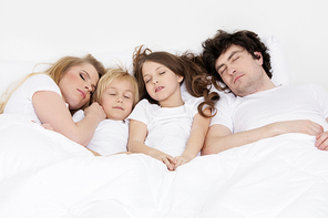 Family with two children sleeping together on a same bed