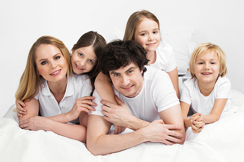 Smiling family with three children wake up in bed