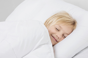 Cheerful smiling blond boy sleep in white bed