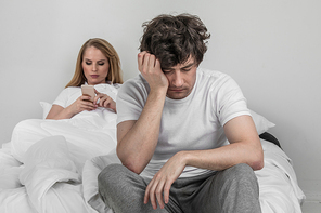 Family conflict concept, addicted to cellphone woman and upset man on bed