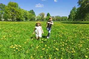 Happy children friends run and play outdoors on yellow dandelion flower meadow