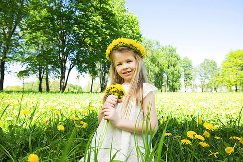 Sweet little girl with floral head wreath on and flowers bunch in hands in summer park