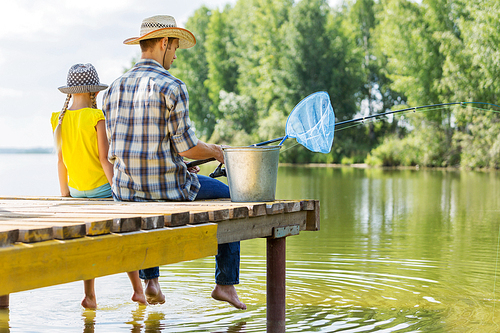 Rear view of father and daughter sitting on bridge and fishing