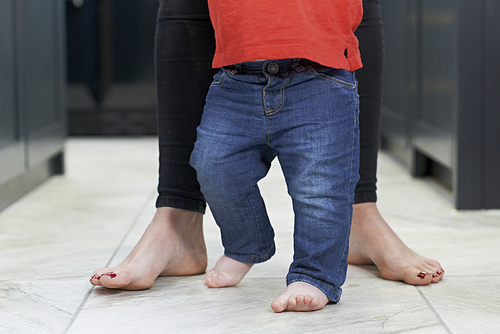 Close Up Of Mother Helping Baby Son To Walk In Kitchen