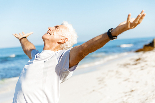 Handsome man in sport wear with outstretched arms standing on beach