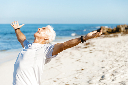 Handsome man in sport wear with outstretched arms standing on beach