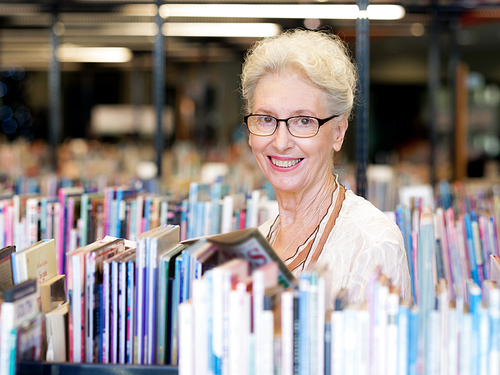 Elderly lady standing next to book shelves in library