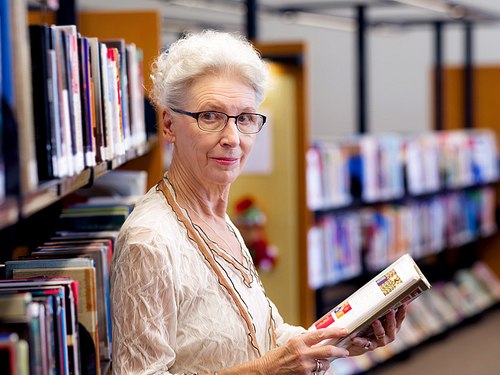 Elderly lady standing next to book shelves in library