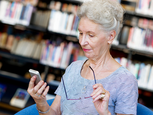 Elderly lady with mobile phone in library