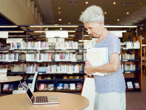 Elderly lady standing next to table with laptop