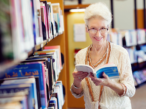 Elderly lady standing next to book shelves in library