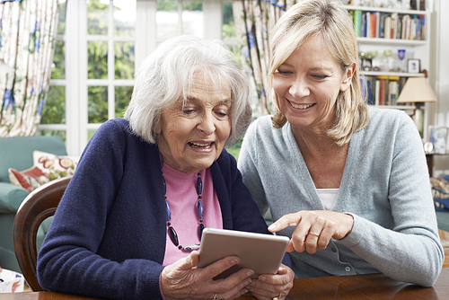 Female Neighbor Showing Senior Woman How To Use Digital Tablet