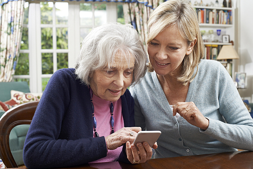 Woman Helping Semior Neighbor To Use Mobile Phone