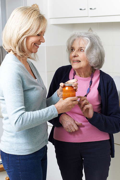 Woman Helping Senior Neighbor To Remove Jar Lid