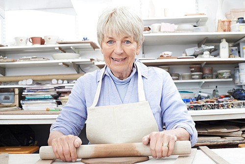 Portrait Of Senior Woman Rolling Out Clay In Pottery Studio