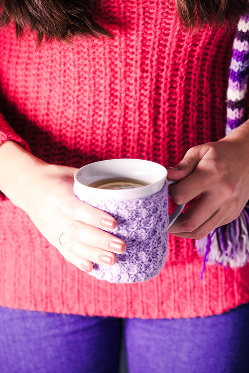 Woman is holding a knitted cup of tea with lemon