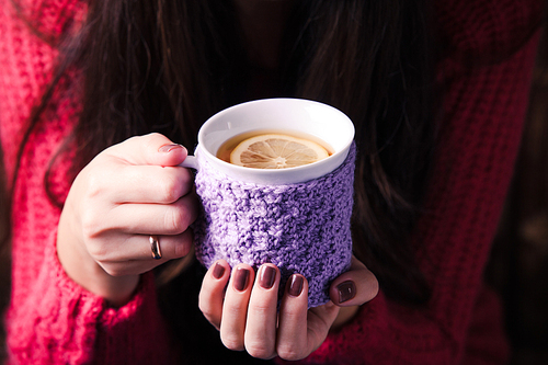 Woman is holding a knitted cup of tea with lemon