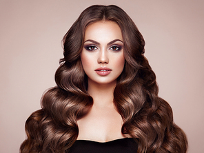 Brunette Girl with Long Healthy and Shiny Curly Hair. Care and Beauty. Beautiful Model Woman with Wavy Hairstyle. Make-Up and Black Dress