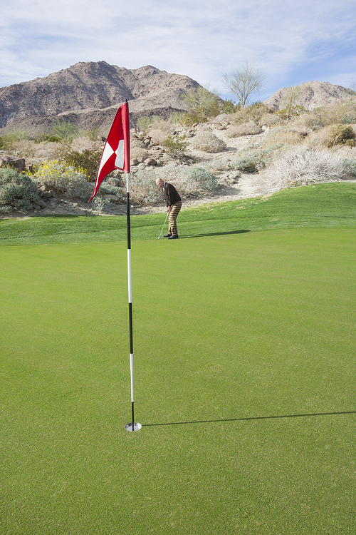 Senior man playing golf with flag in foreground