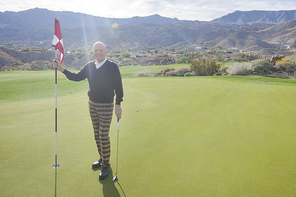 Full length portrait of happy senior male golfer holding flag and putter at golf course