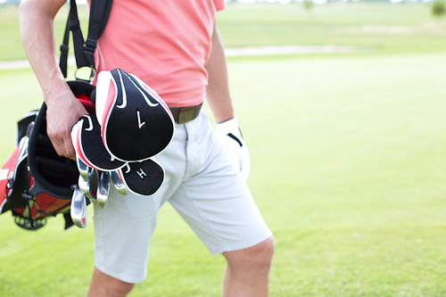 Midsection of man carrying golf club bag at course
