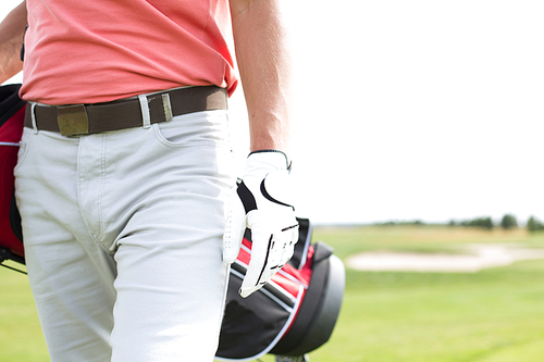 Midsection of man carrying golf club bag while walking at course