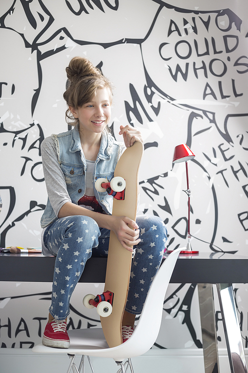 Full-length of girl with skateboard sitting on study table at home