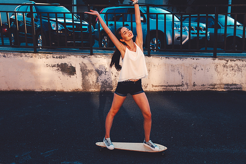 Young woman ride on skateboard in urban setting in happy state celebrate summer freedome with her hands rised outdoors active lifestyle concept