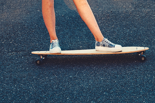 Closeup of skateboarder legs. Woman in sneakers riding skateboard outdoor on asphalt surface. Copyspace on asphalt.