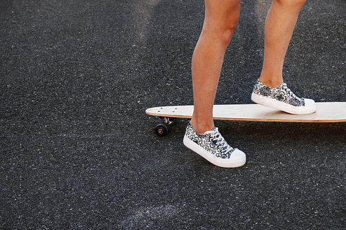 Girl ready to push her skate forward. Close up of girl skateboarder feet while skating in the park on asphalt surface, shot with a lot of copyspace.