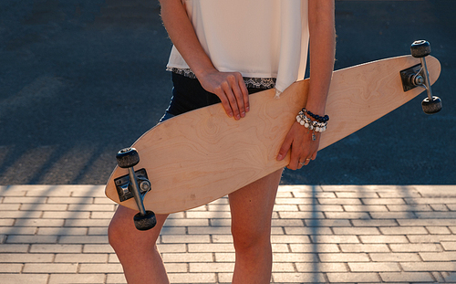 Front view of young girl in shorts holding longboard by both hands. Skateboard Extreme Sport Skater Activity Concept. Shadow pattern on pavement behind model.