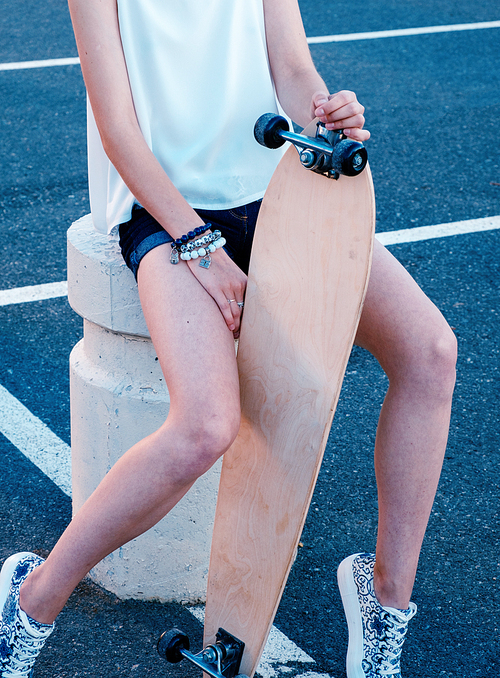 Girl-skater sitting in skate park with her longboard between her bare legs