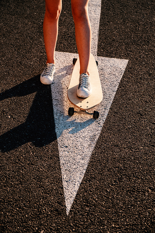 Skater girl is ready to start moving forward, aiming concept. Legs of skater tteen standing on arrow road marking in ready to ride position.