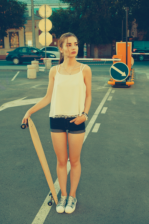 Woman in street vintage fashion wear standing on parking lot in front of road signs and looking away while holding longboard, copyspace on the right side of image