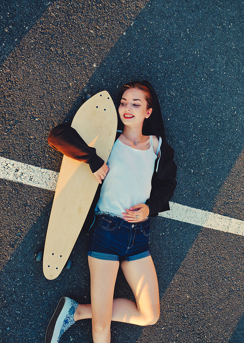 Skater girl lying down on asphalt surface of the road and enjoing summer warm weather after phisical activity, copyspace