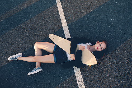 Very tyred skater girl sleeping on asphalt in warm summer day, copyspace