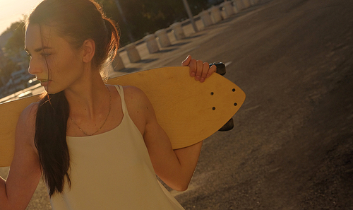Girl with skatedoard behind her shoulders in summer looking away, shot with copyspace