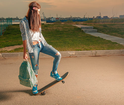 Hipster girl on skateboard with backpack in her hands