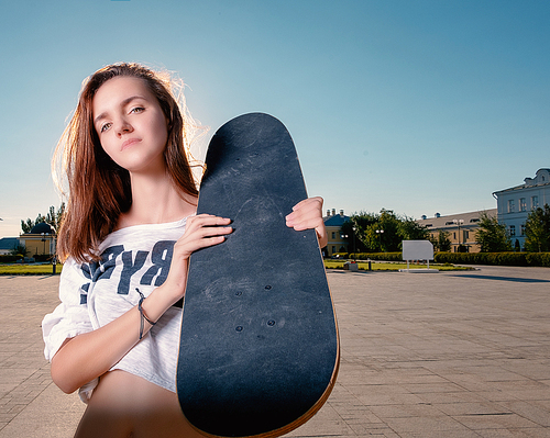 Wide angle shot of skater girl with skateboard on her shouler, a lot of space for text on the sky