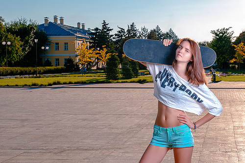 Sporty girl in short shirt showing her bare belly posing with skateboard on her shoulder,  with blank expression, a lot of space for text.