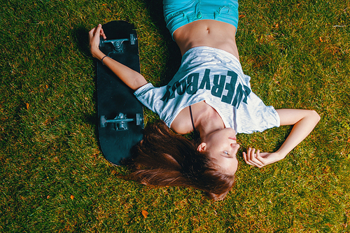 Teen Girl skater resting on grass with her skateboard near top view